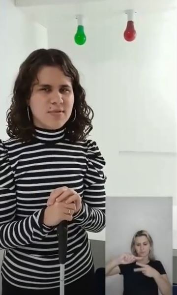 Imagem retirada do vídeo, que mostra a aluna Júlia Victória Pereira em pé no Laboratório de Análises Sensoriais. No canto direito, está a tela com a intérprete de Libras, Marizete Darmorus Pereira.