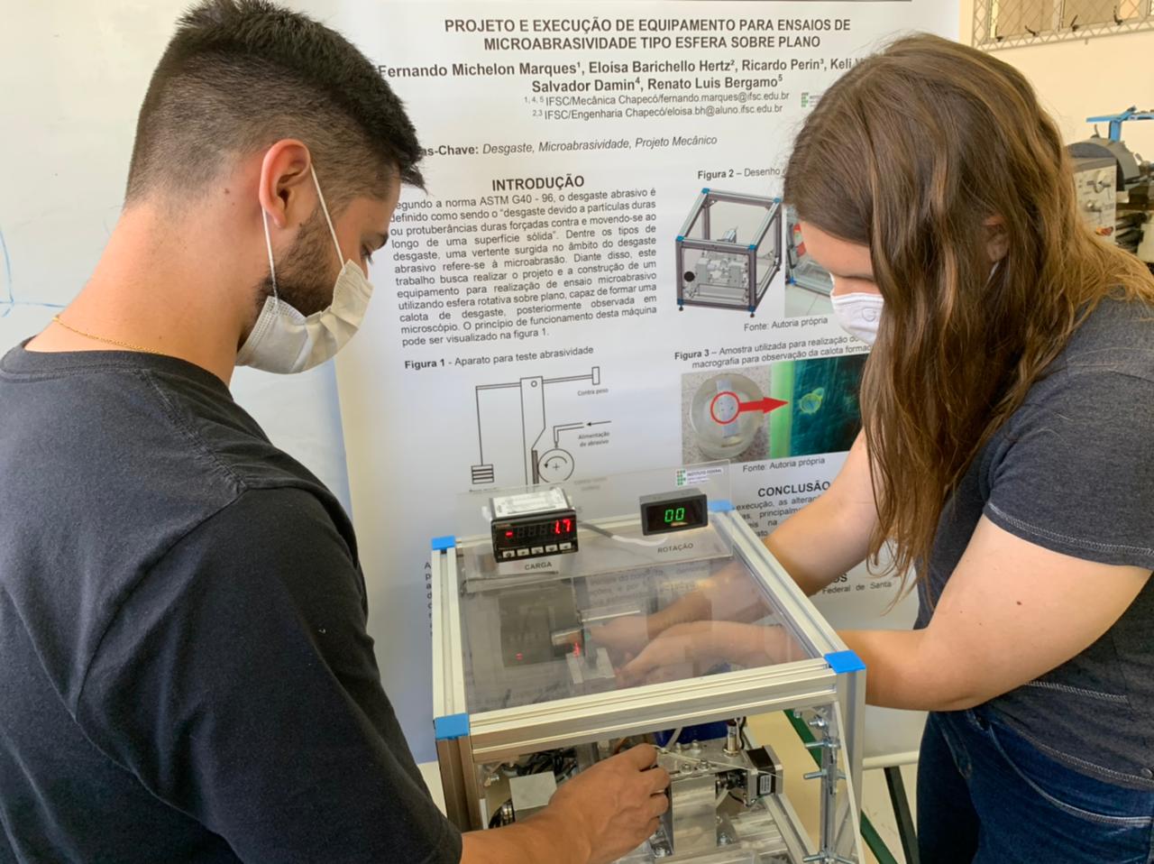 Estudantes Eloísa Hertz e Ricardo Perin com o equipamento para ensaios de microbrasividade tipo Esfera Sobre Plano